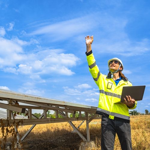 Engineer launching a drone for solar panel inspection in a solar farm under a vibrant blue sky. Equipped with laptop, reflective jacket, and helmet, showcasing modern technology in renewable energy.